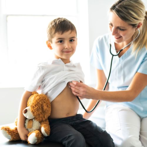 Lekarka Poradni Na Dubiela w Zabrzu osłuchująca małe dziecko podczas wizyty pediatrycznej, z misiem w rękach pacjenta.
